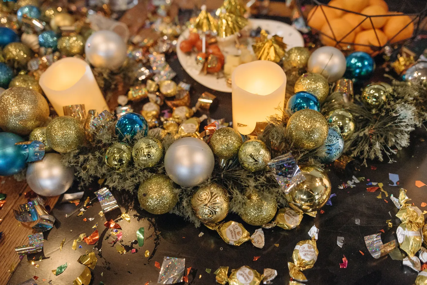 Cozy festive table setting with candles, Christmas ornaments, and confetti for holiday celebrations.
