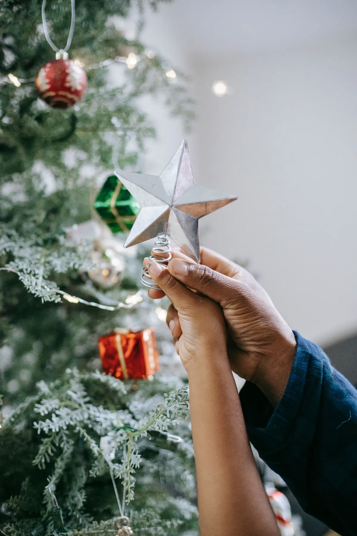 Crop anonymous African American dad and kid decorating fir tree with star during Christmas preparation
