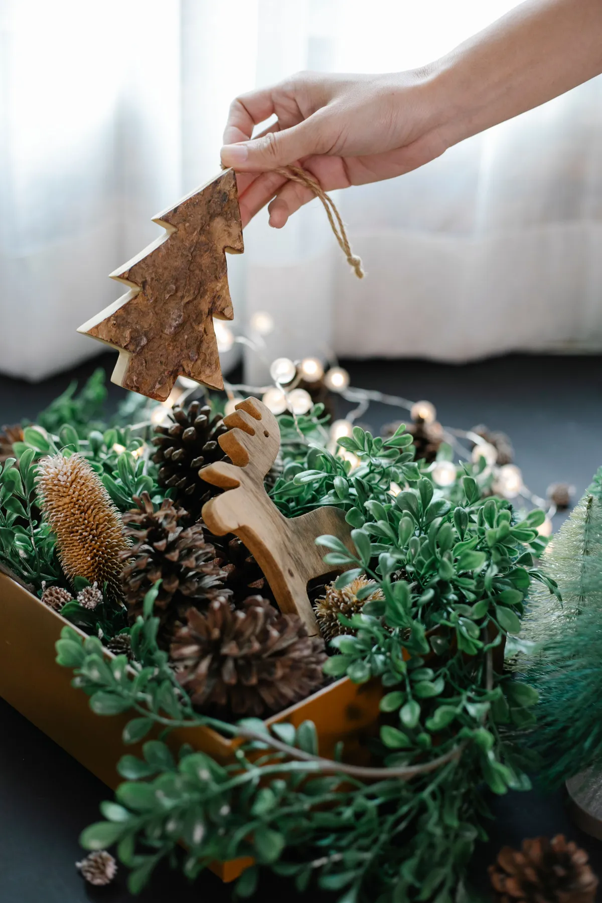 Crop anonymous person putting small Christmas decorations in box placed in light room in daylight