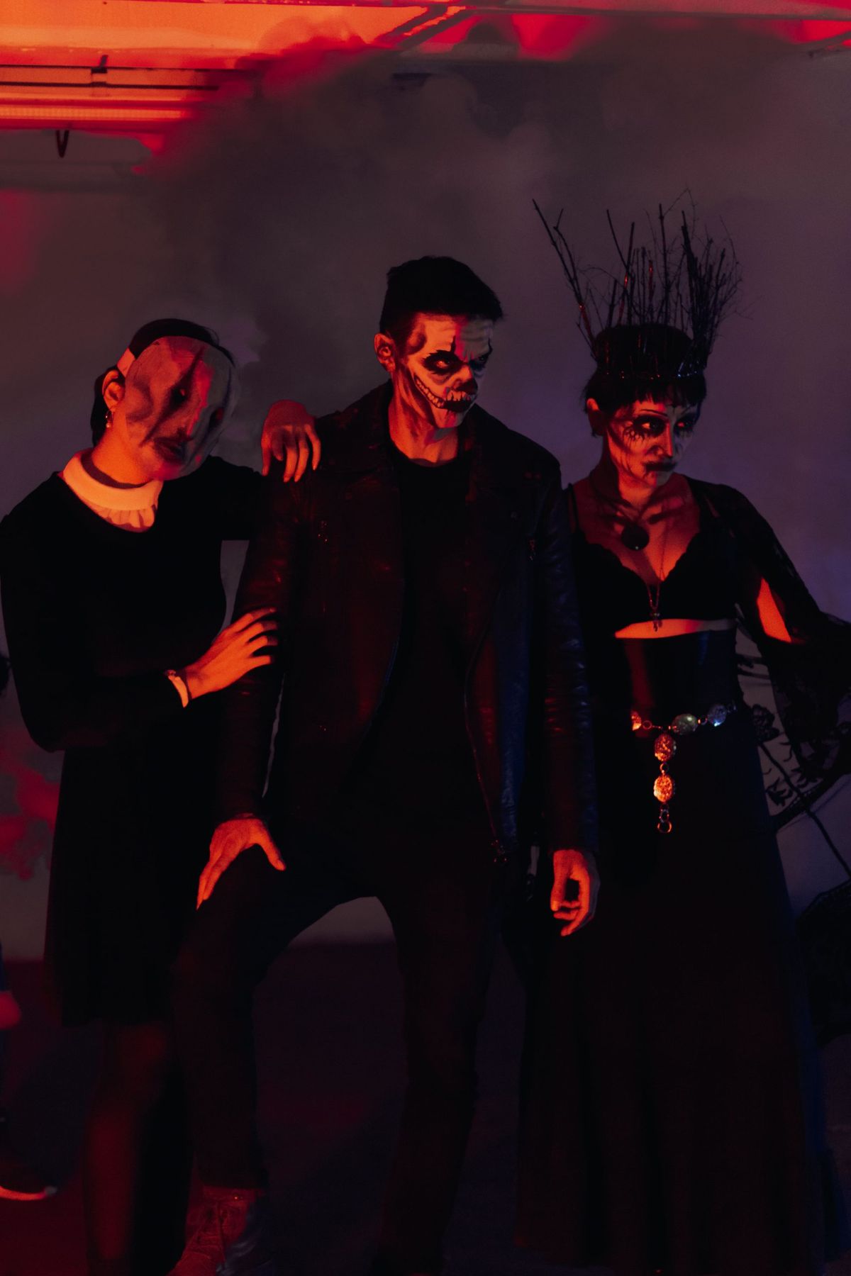 Dark and moody portrait of three adults in Halloween costumes, with dramatic lighting.