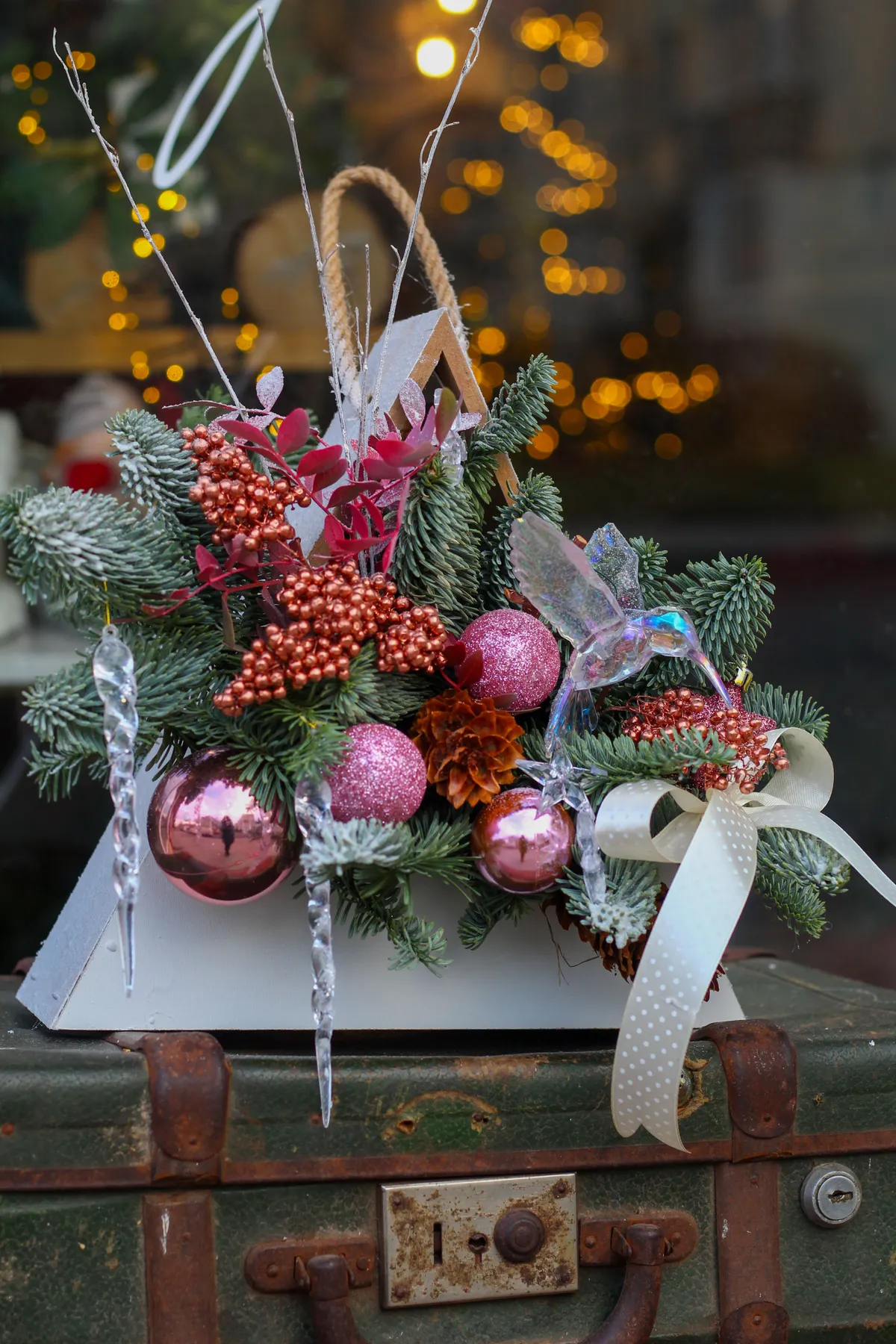 Elegant Christmas floral decoration with pink ornaments and ribbon on vintage suitcase.