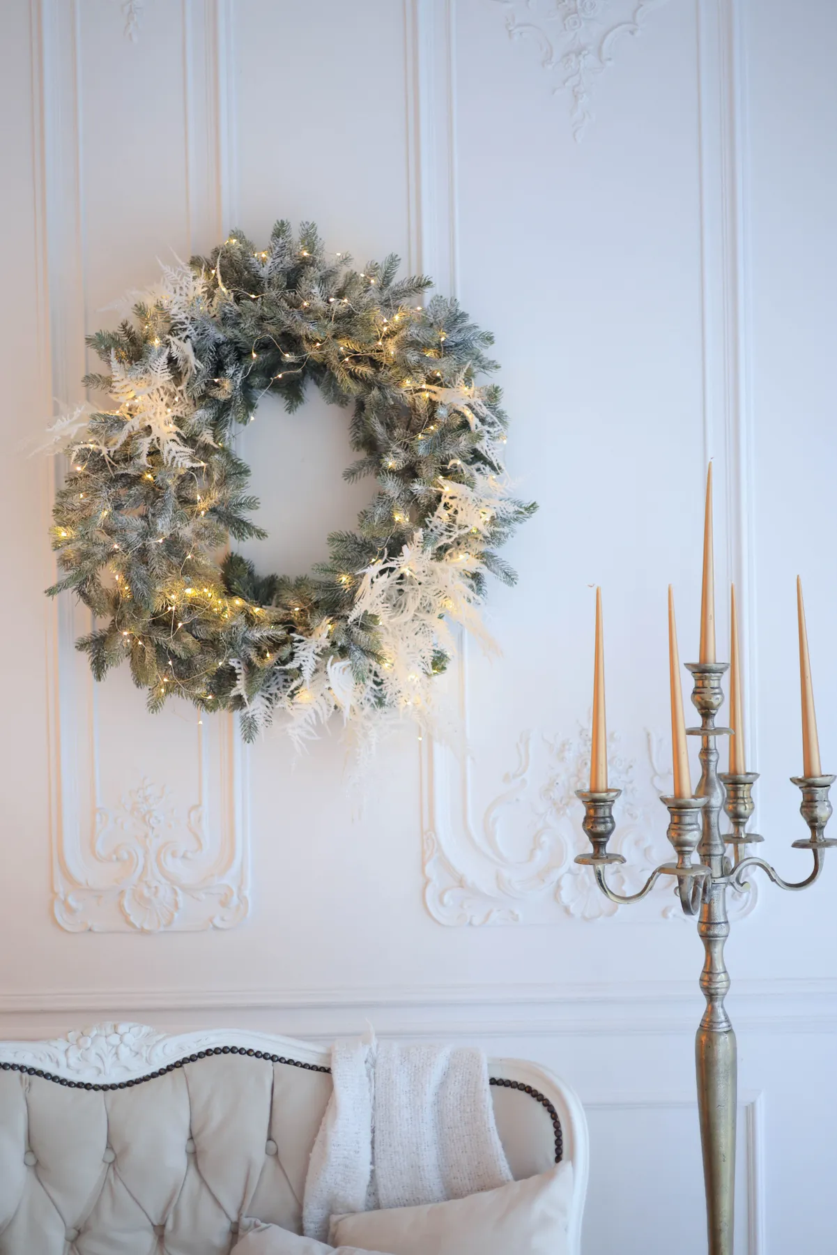Elegant Christmas wreath on white wall with candle holder, creating a festive ambiance.