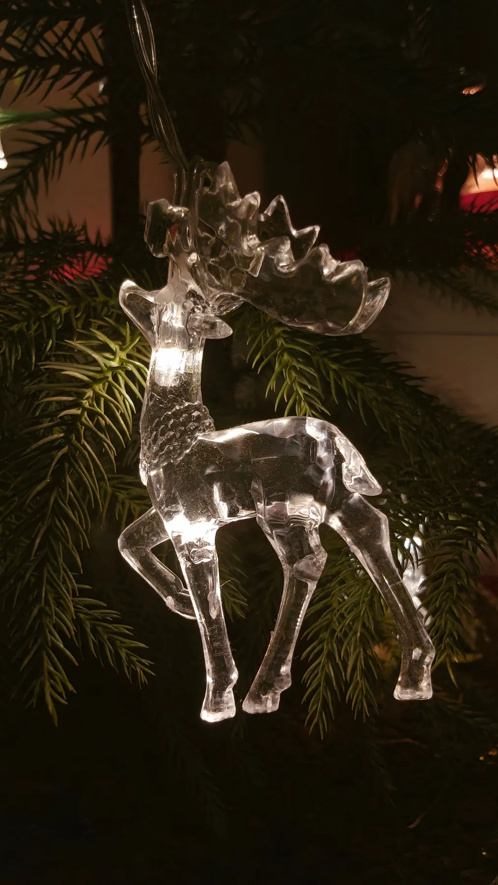 Elegant glass reindeer ornament sparkling among festive foliage, perfect for holiday decor.