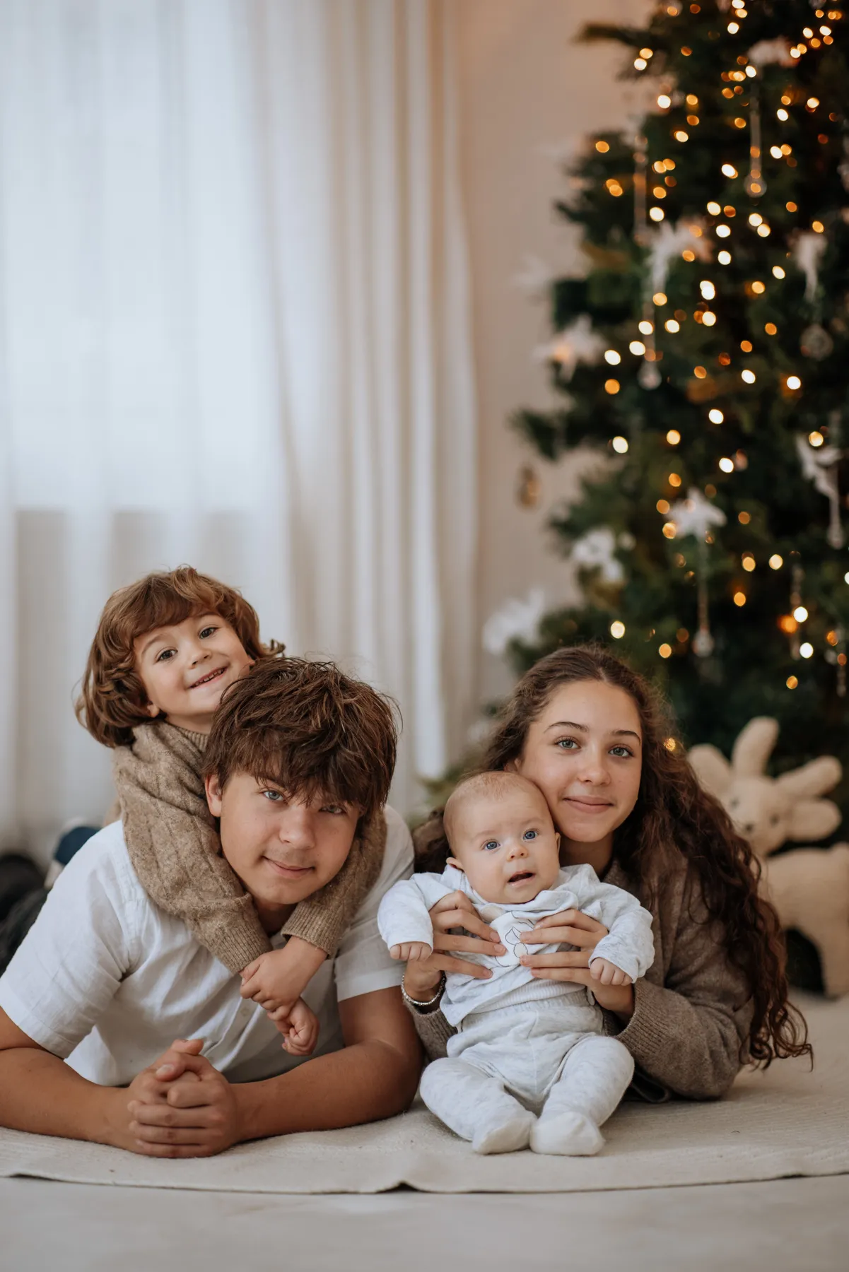Family enjoys Christmas time together indoors with a decorated tree and festive lights.