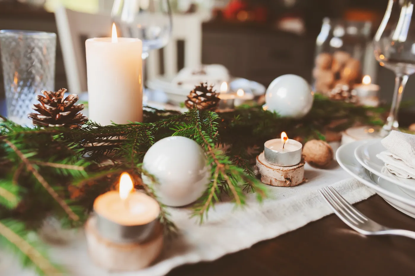 Festive Christmas and New Year table setting in scandinavian style with rustic handmade details in natural and white tones. Dining place decorated with pine cones, branches and candles - domicilis.n