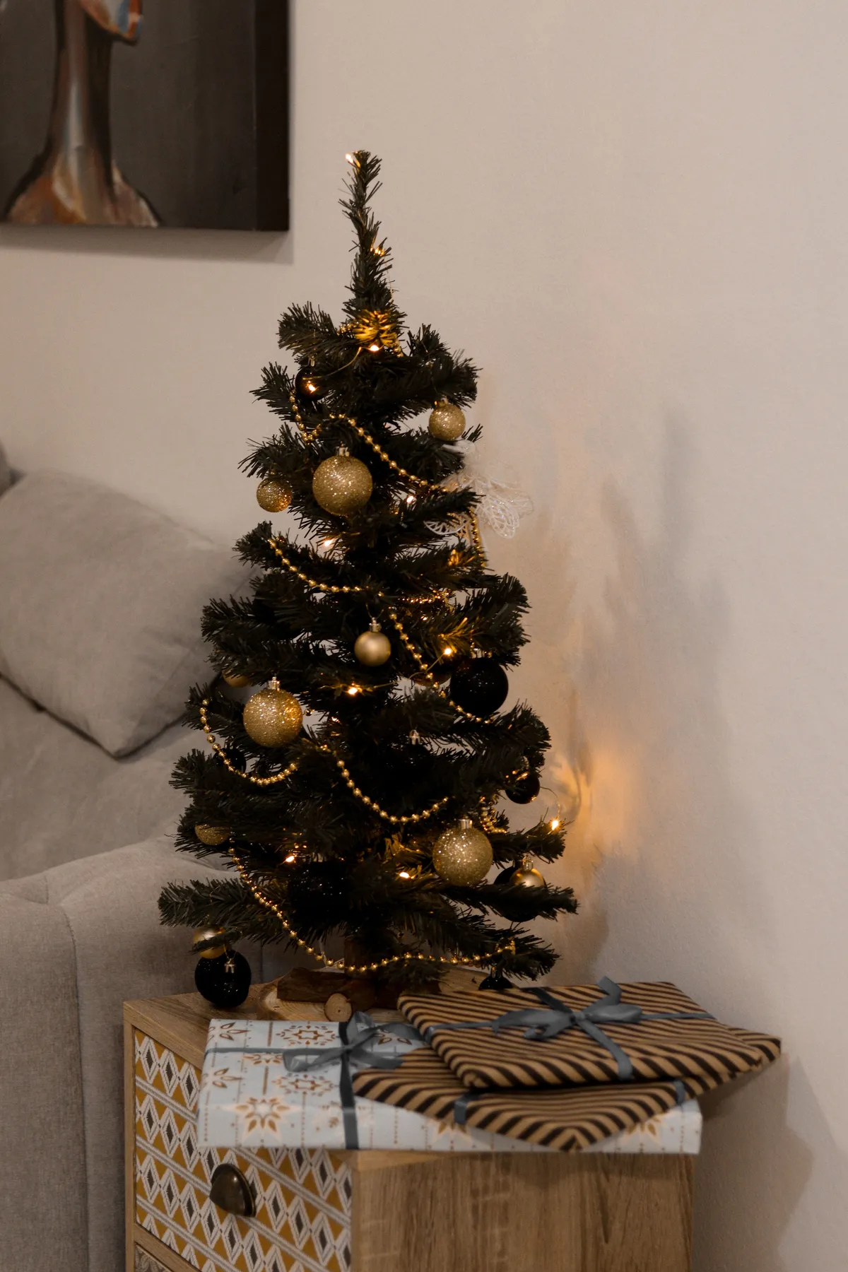 Festive Christmas tree with ornaments and wrapped gifts beside a cozy sofa.