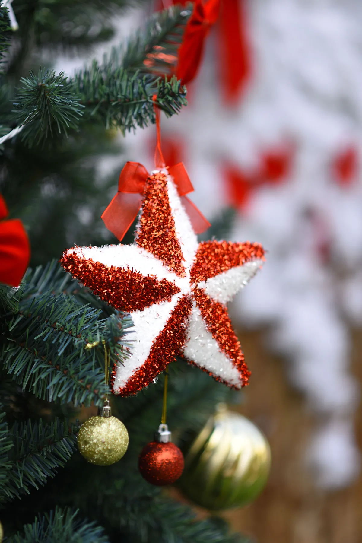 Festive red and white star ornament with baubles on a decorated Christmas tree branch.