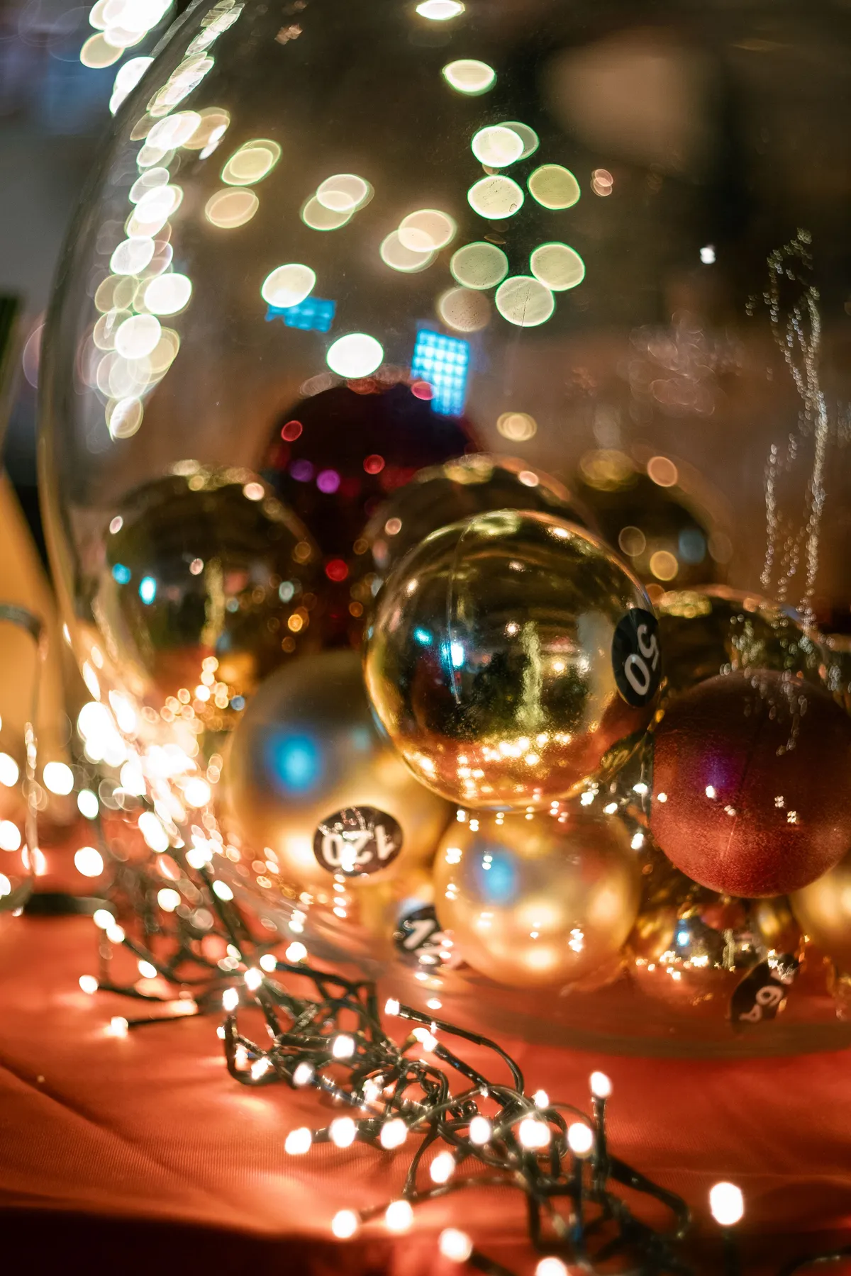 Golden and red Christmas ornaments in a glass bowl, surrounded by glowing fairy lights.