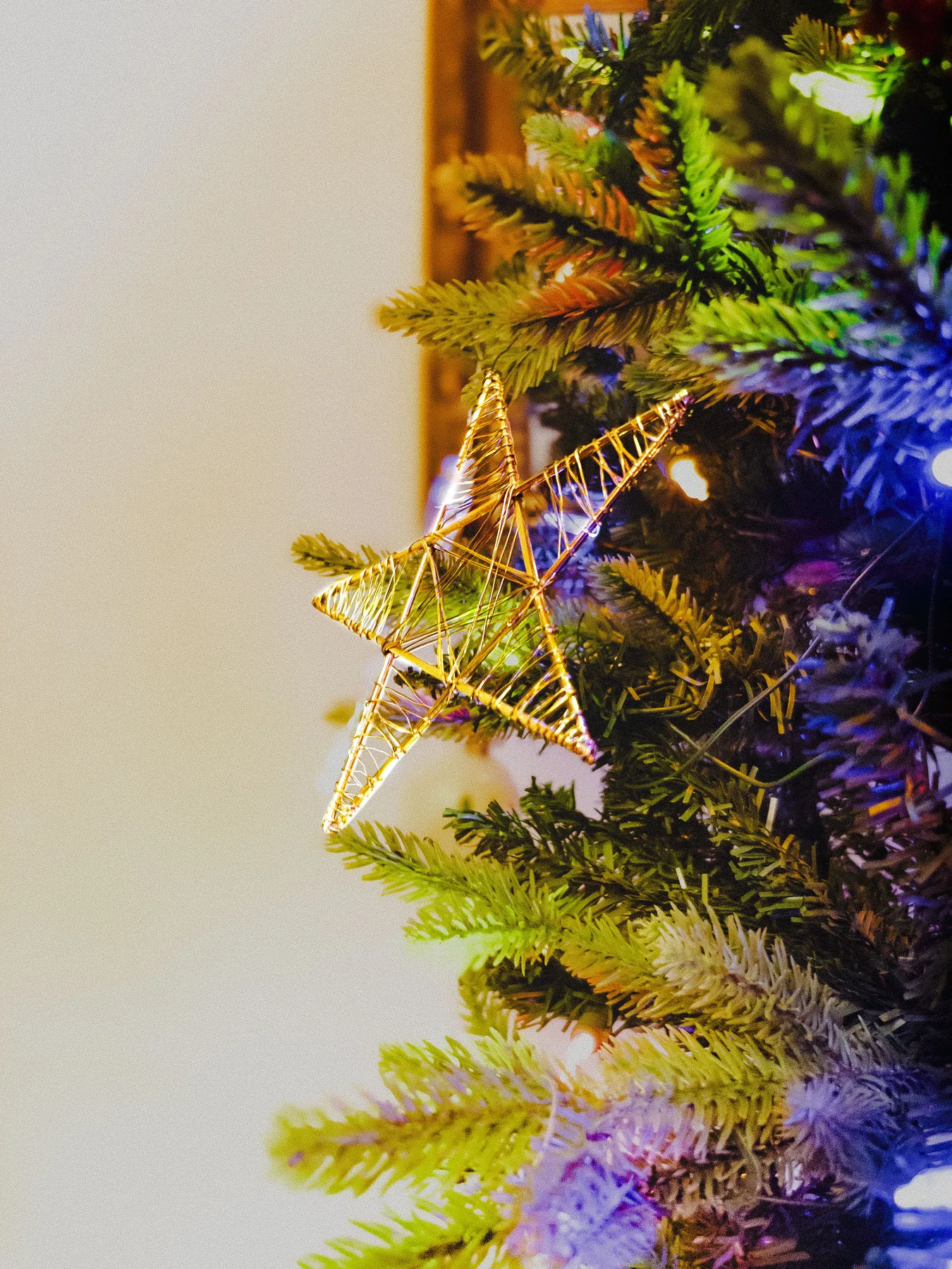 Golden star ornament hanging on a lush decorated Christmas tree branch.