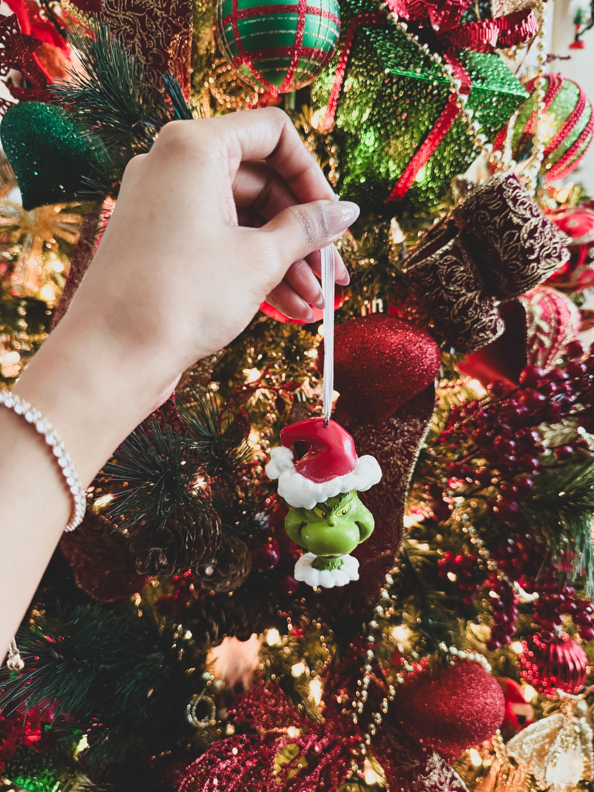 Hand placing Santa and Grinch ornament on decorated Christmas tree.