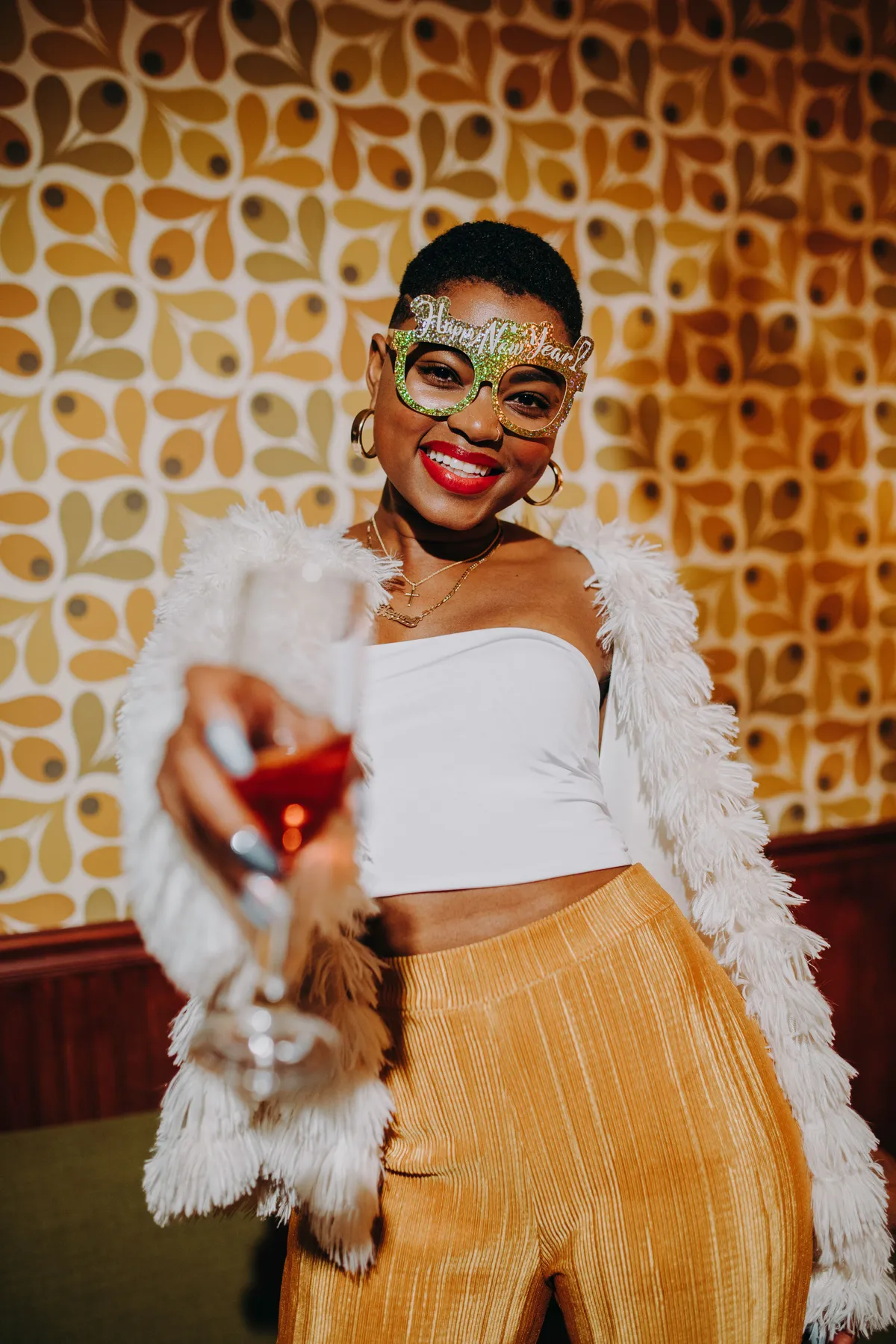 Happy woman celebrating New Year's Eve with champagne, wearing festive glasses and smiling.