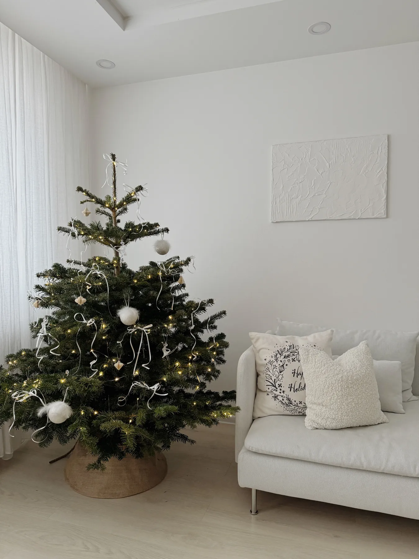 Minimalist Christmas tree with white decorations in a bright living room.
