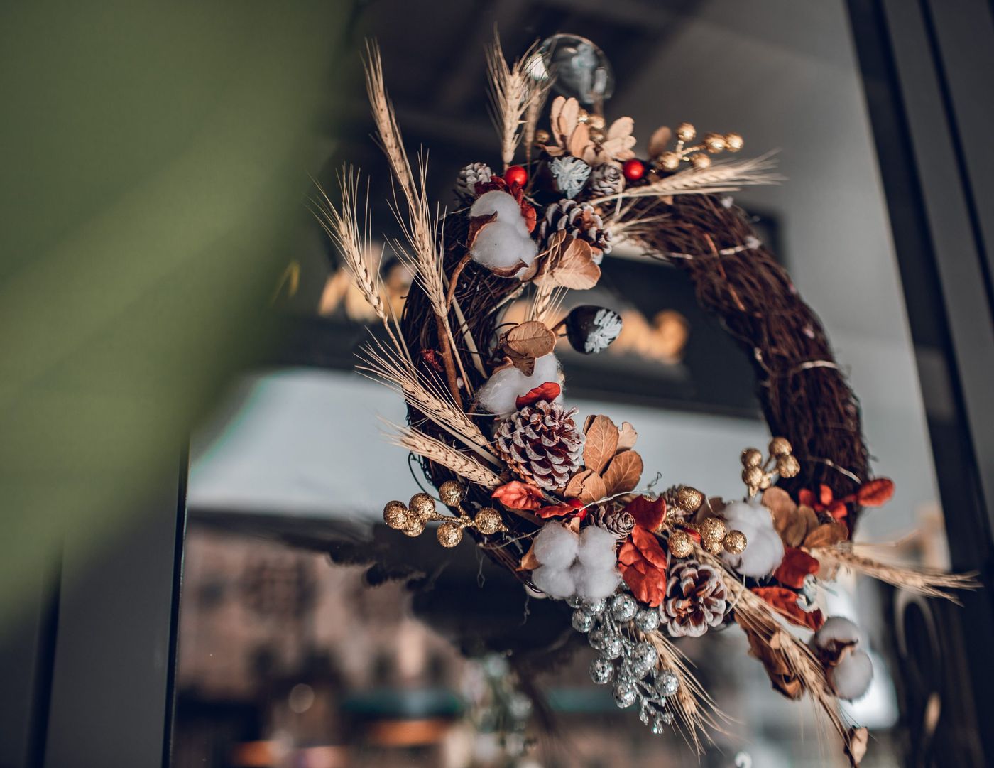 Ornate holiday wreath with pine cones and cotton on a glass door, perfect for festive decor.