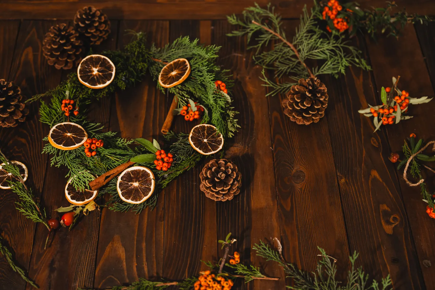 Rustic wreath with pinecones, dried citrus, and red berries on wooden background.