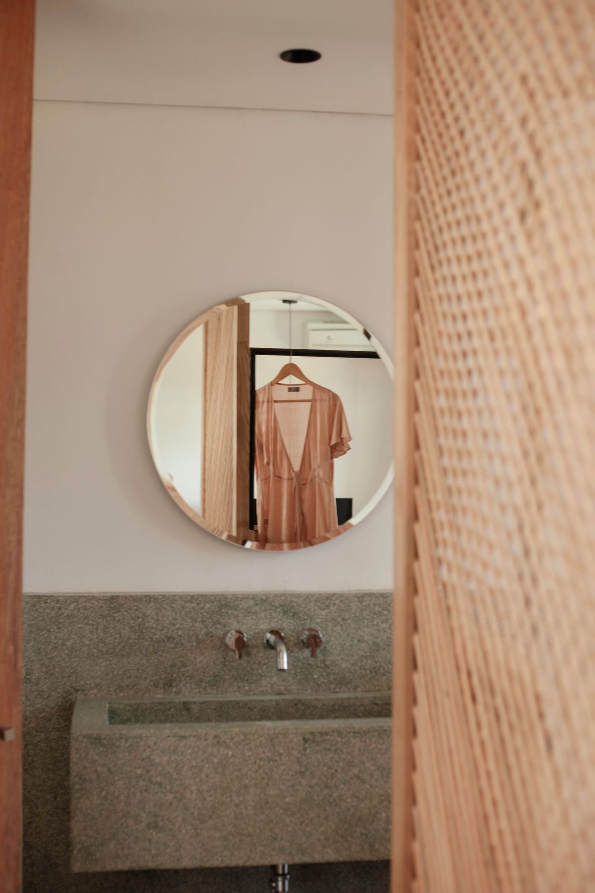 Stylish dress hangs reflected in a round mirror, enhancing a modern bathroom's minimalist decor.