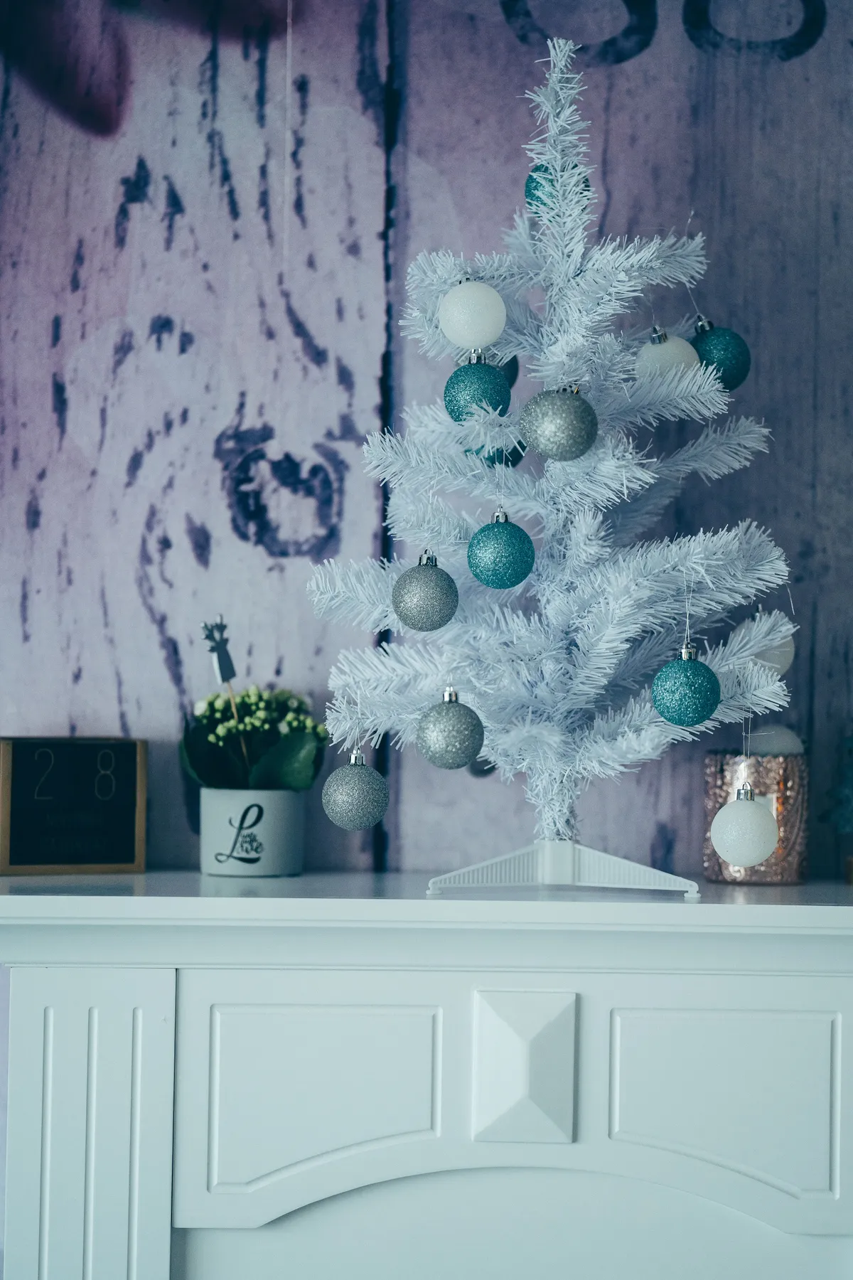 Stylish white Christmas tree decorated with teal and silver ornaments on a mantel.