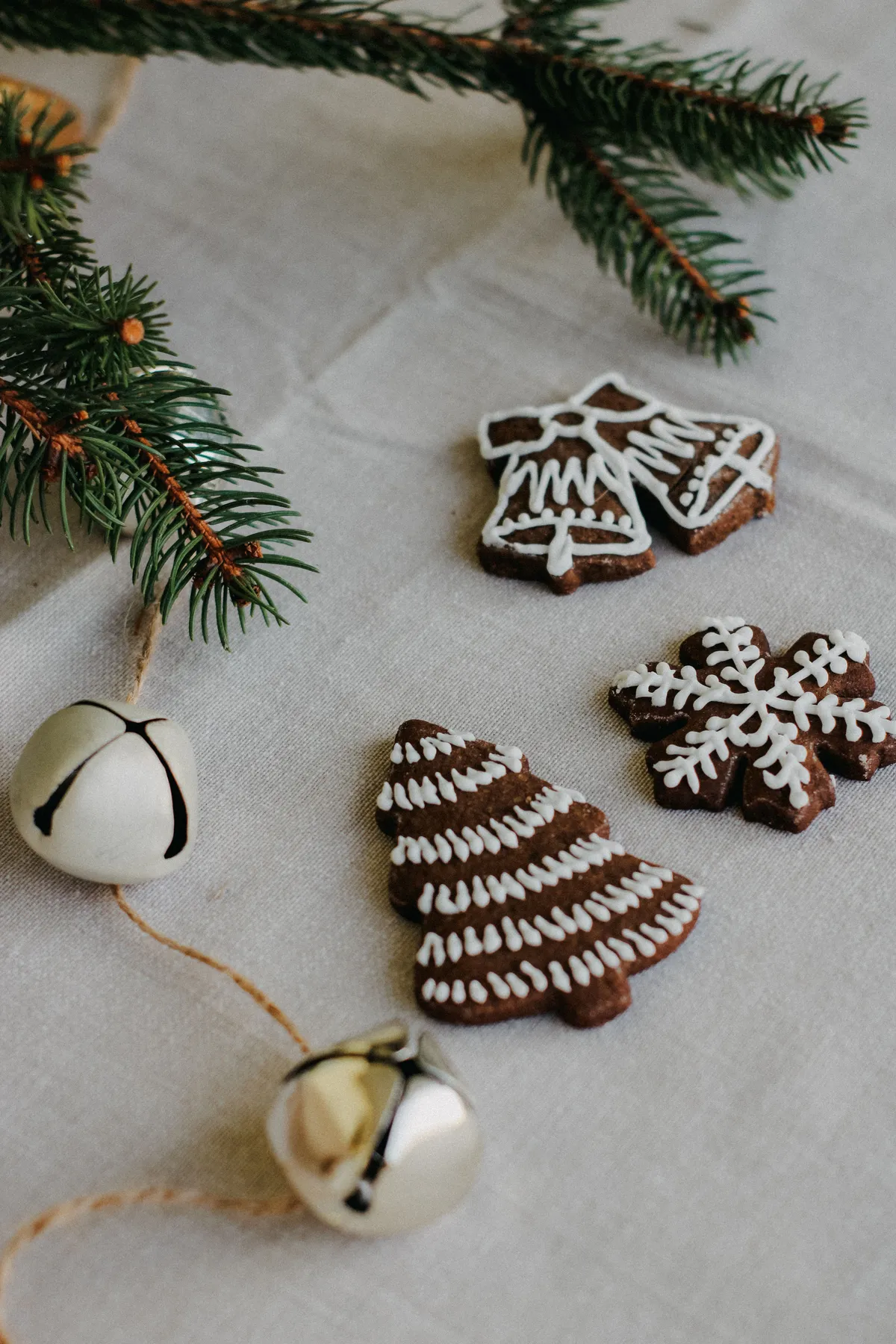 Three decorative gingerbread cookies with icing, complemented by holiday bells and pine branches.