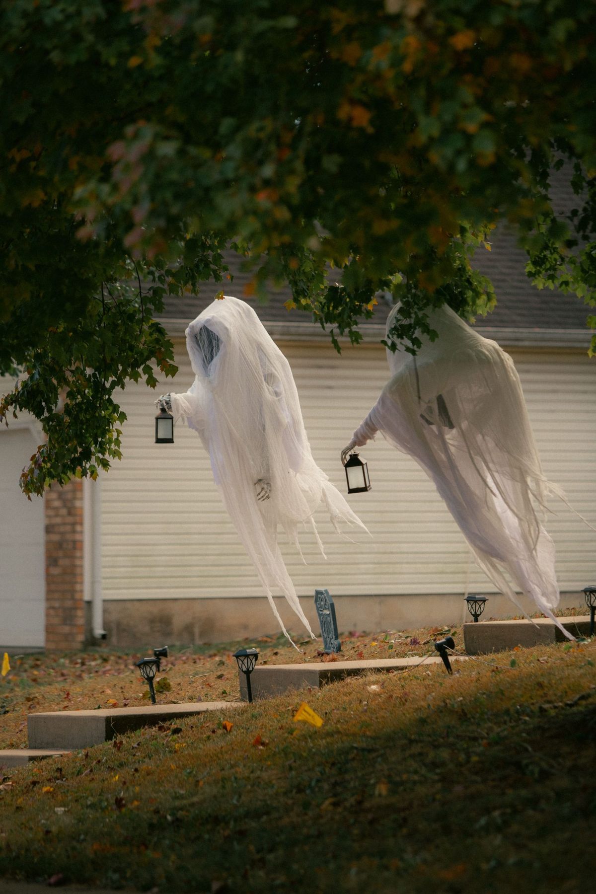 Two ghost figures hanging from trees in a garden, creating a spooky Halloween scene.