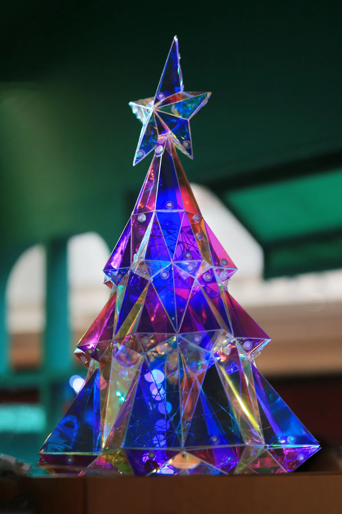 Vibrant glass crystal Christmas tree with star topper, illuminated by colorful lights.
