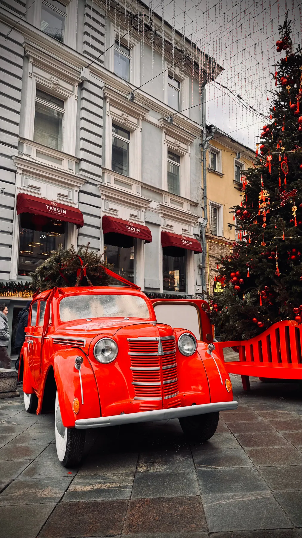 Vintage red car with Christmas tree and decorations in city setting, perfect for holiday themes.
