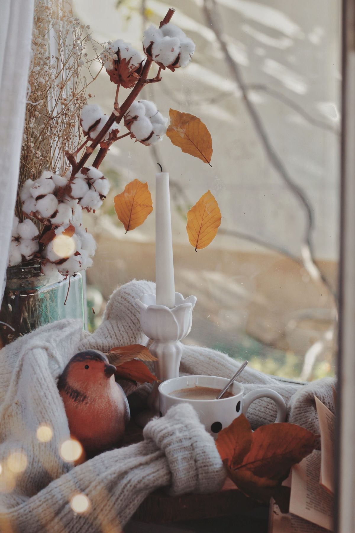 Warm autumn scene with a candle, coffee, and leaves for cozy vibes.