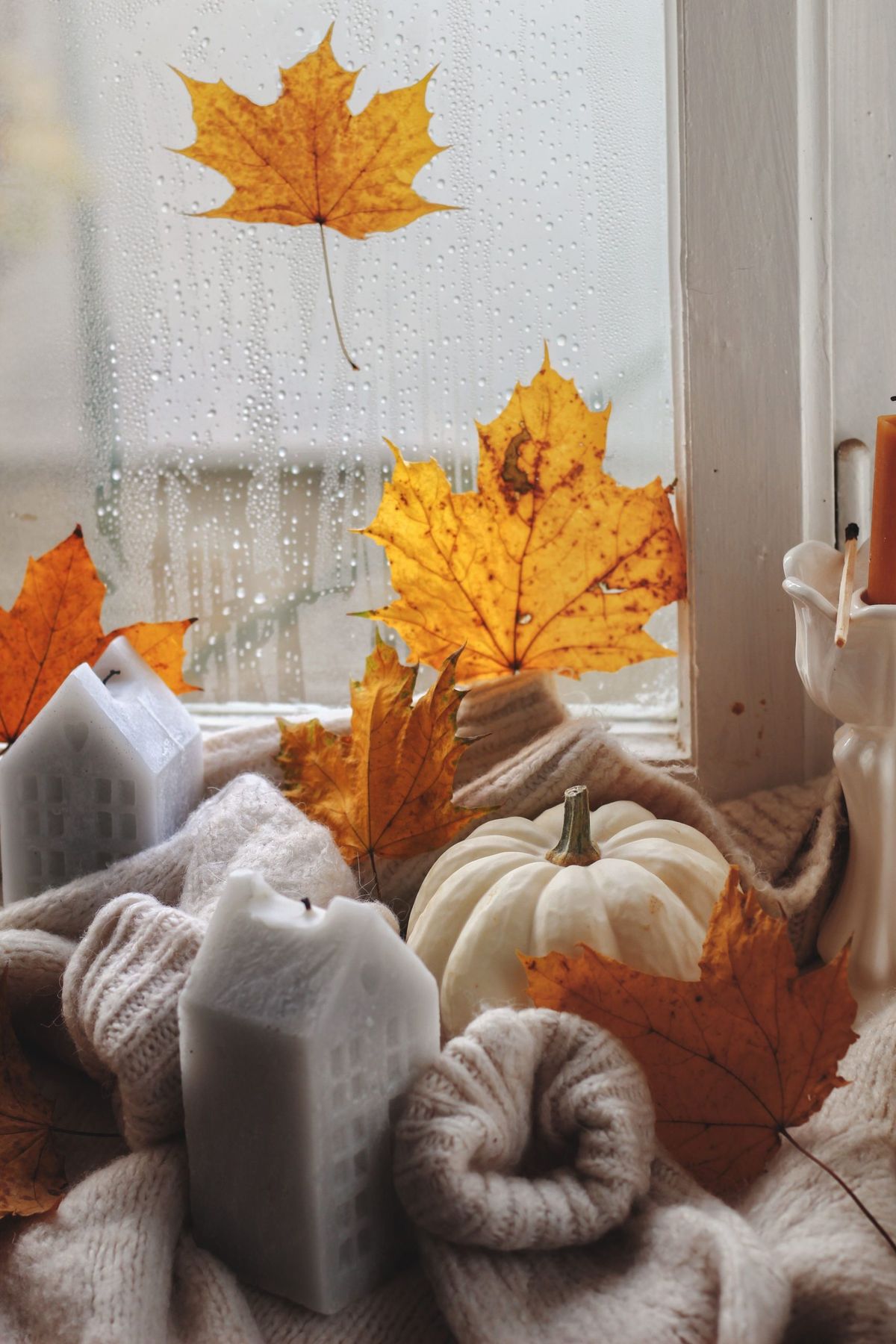 Warm autumn scene with candles, leaves, and pumpkin on a windowsill.