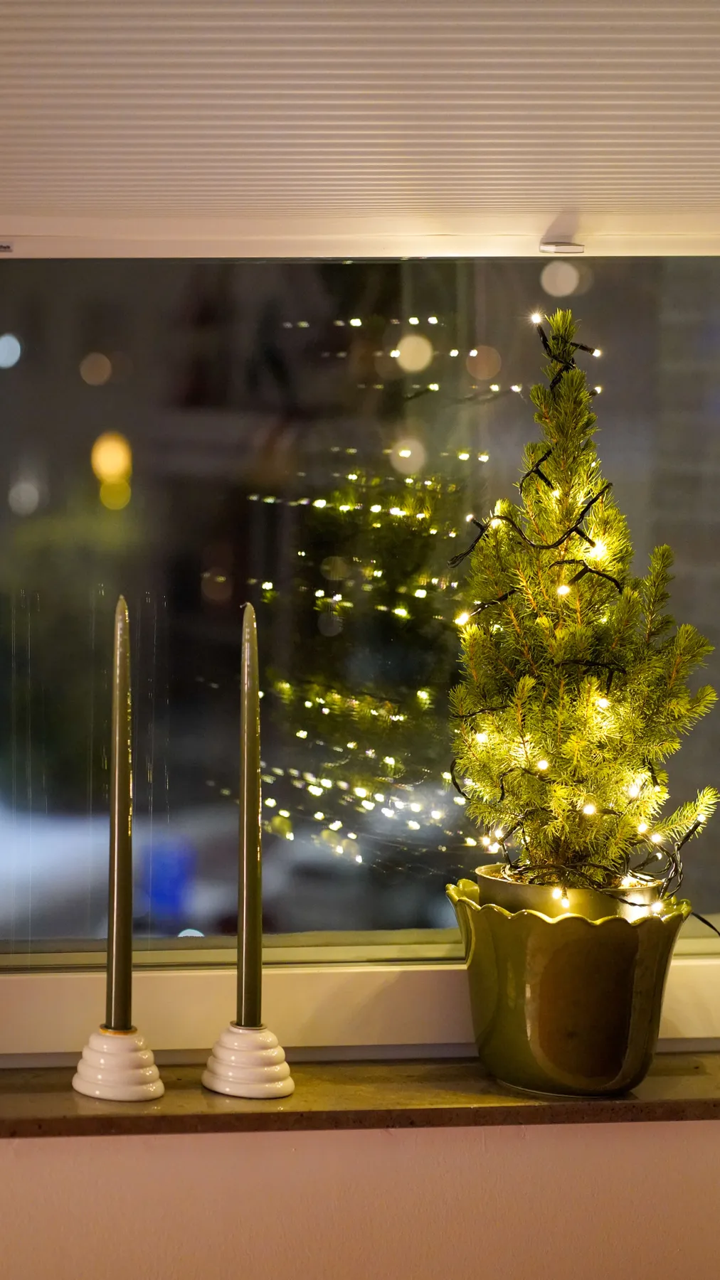 Warm holiday scene featuring a small Christmas tree with lights and candles by the window.