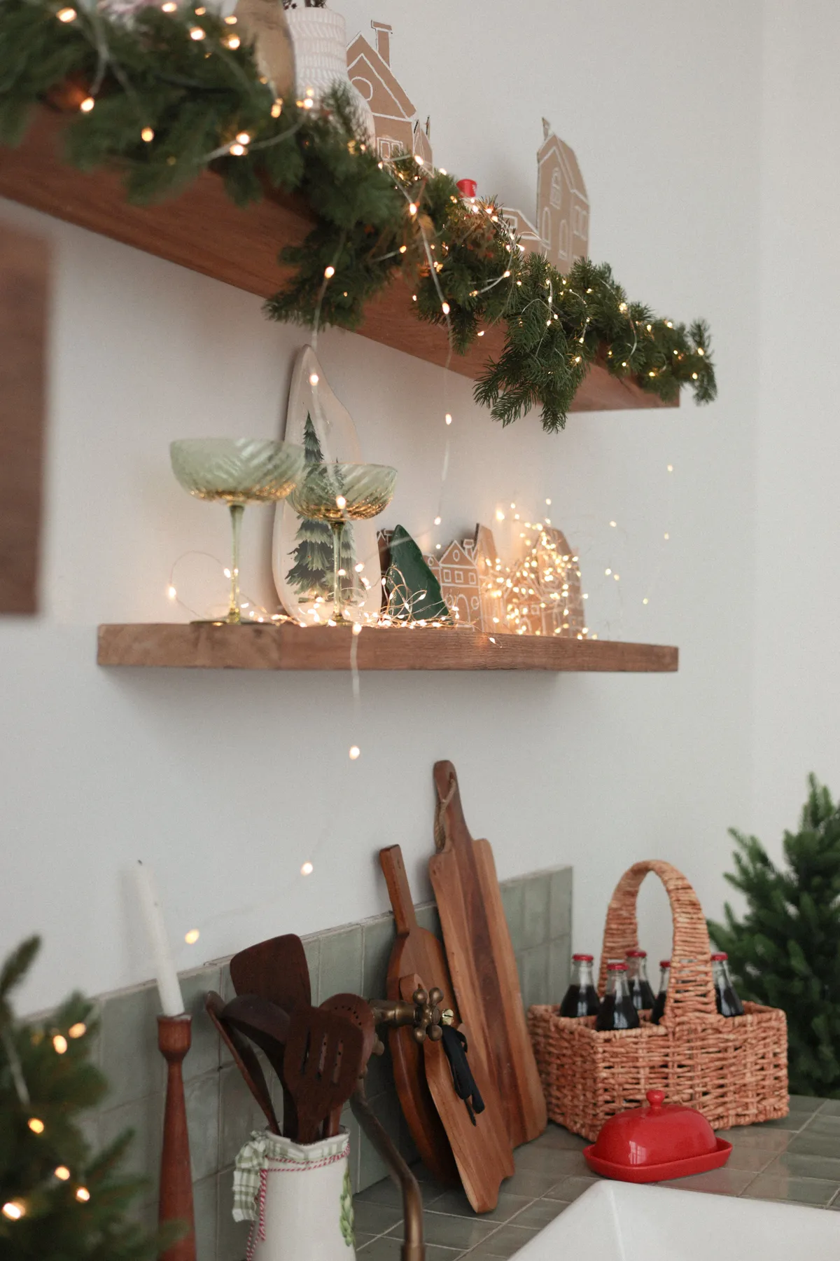 Warm kitchen shelves decorated with holiday lights and greenery, evoking a festive atmosphere.
