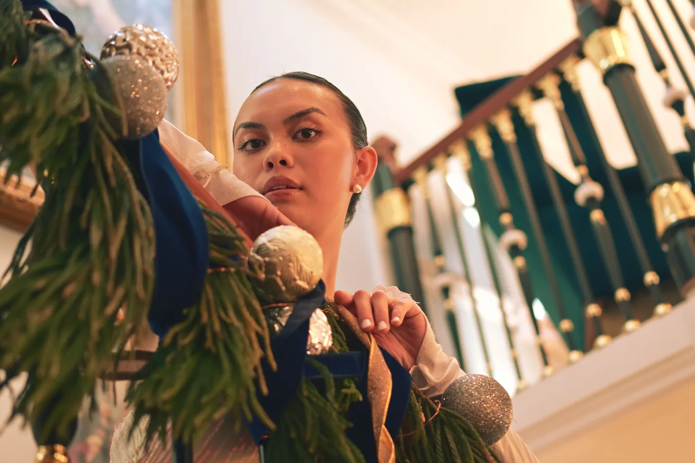 Woman decorates staircase with festive garland adorned with silver ornaments.