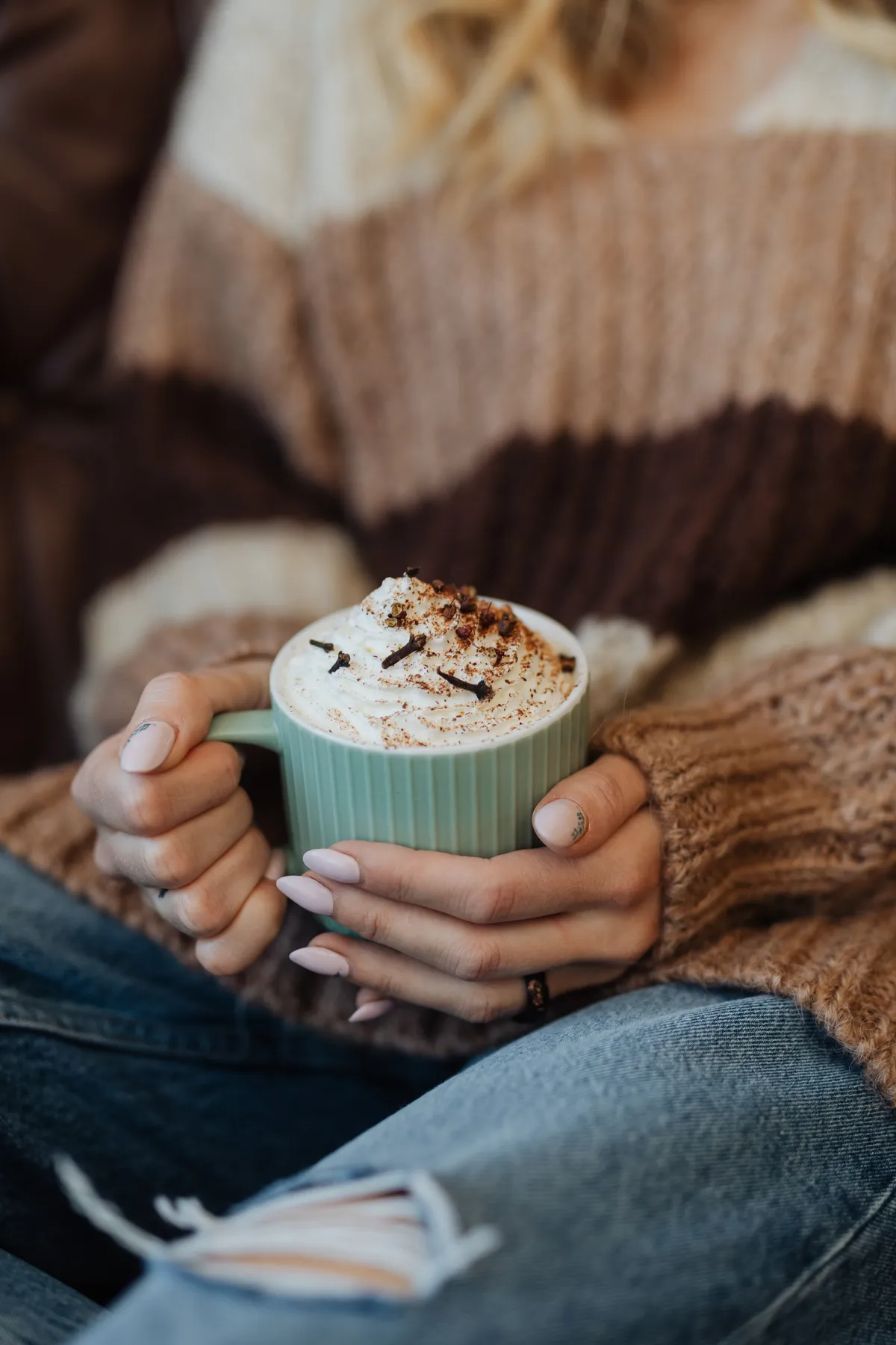 Woman holding a comforting hot chocolate with whipped cream on a fall day.