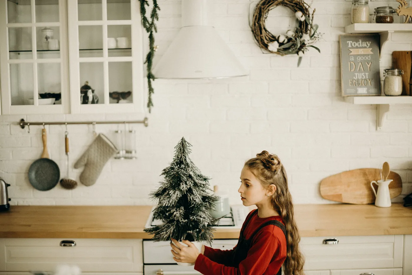 Young girl decorating a cozy kitchen with a mini Christmas tree, capturing the holiday spirit indoors.